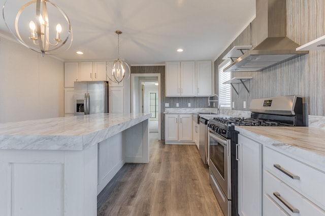 kitchen featuring pendant lighting, a center island, wall chimney exhaust hood, appliances with stainless steel finishes, and white cabinetry