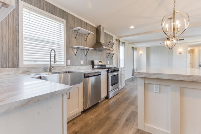 kitchen featuring wall chimney exhaust hood, stainless steel appliances, sink, pendant lighting, and light hardwood / wood-style floors