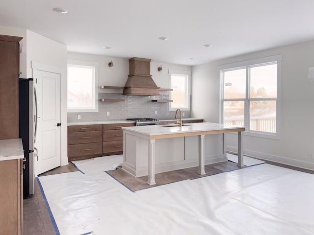 kitchen featuring premium range hood, stainless steel appliances, a center island with sink, a breakfast bar area, and sink