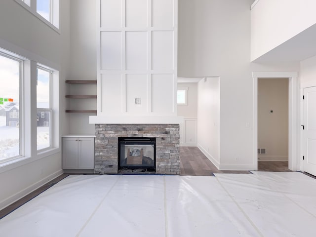 unfurnished living room with hardwood / wood-style floors, a stone fireplace, and a high ceiling