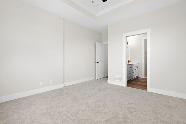 unfurnished bedroom with dark carpet, a raised ceiling, and baseboards