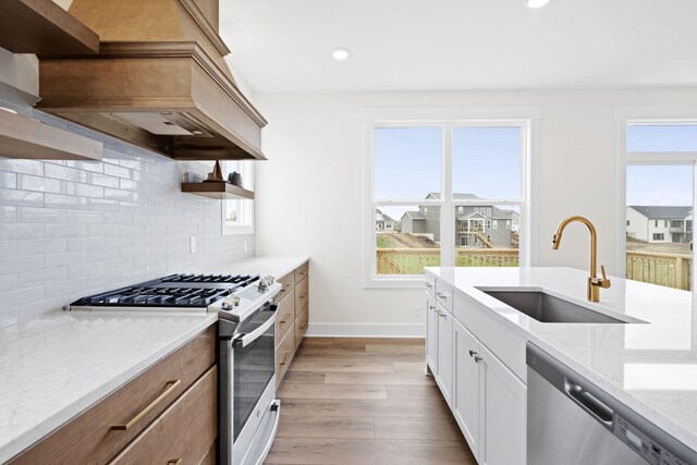 kitchen with stainless steel appliances, a sink, open shelves, decorative backsplash, and light wood-style floors