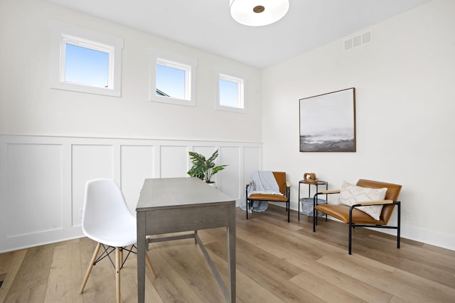 office area featuring a decorative wall, light wood finished floors, and wainscoting