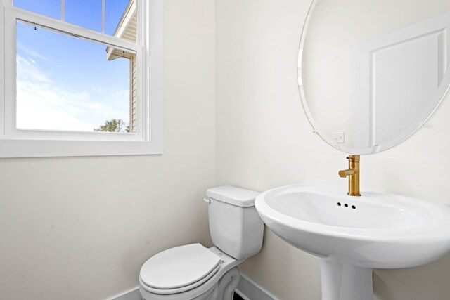 half bath featuring toilet, a sink, and baseboards