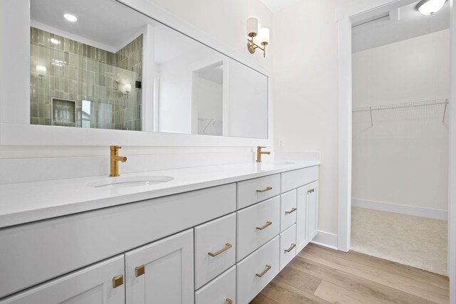 full bathroom featuring a tile shower, double vanity, a spacious closet, wood finished floors, and baseboards