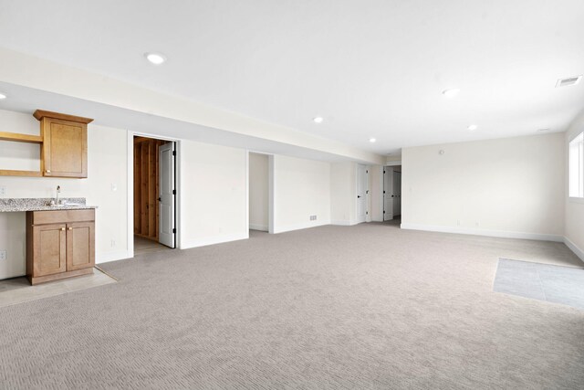 unfurnished living room featuring bar with sink, recessed lighting, light carpet, and baseboards