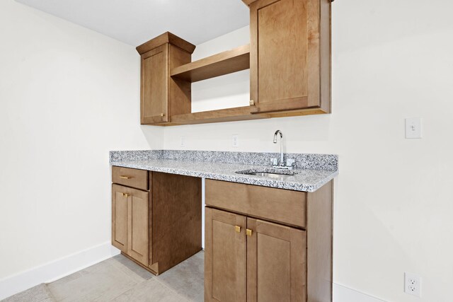 kitchen featuring a sink, open shelves, baseboards, and light stone countertops