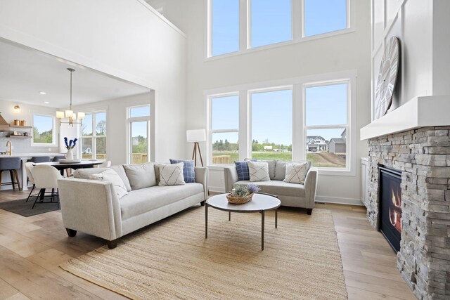 living area with plenty of natural light, light wood-style floors, a fireplace, a chandelier, and a high ceiling