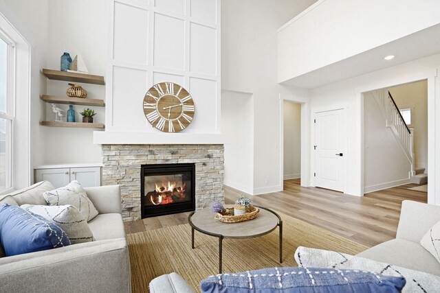 living area with light wood-type flooring, stairway, a stone fireplace, baseboards, and a towering ceiling
