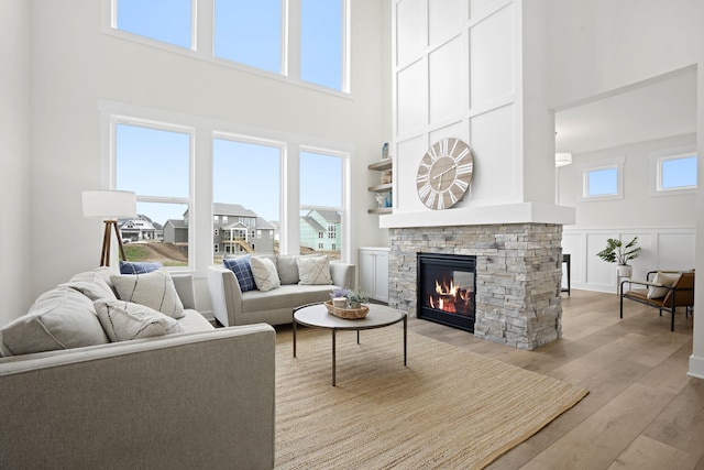 living room featuring light wood-style floors, a towering ceiling, a stone fireplace, a decorative wall, and a wainscoted wall