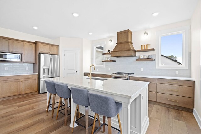 kitchen featuring appliances with stainless steel finishes, premium range hood, a sink, open shelves, and a breakfast bar area
