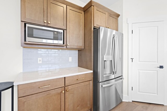 kitchen featuring appliances with stainless steel finishes, backsplash, light wood-style flooring, and light stone counters