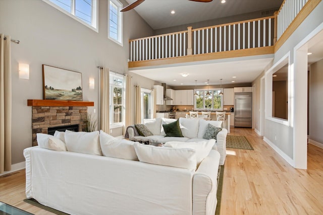 living room featuring baseboards, a towering ceiling, ceiling fan, light wood-style floors, and a fireplace