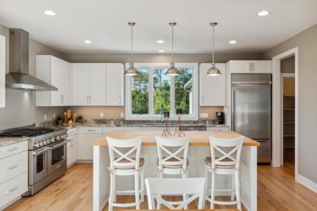 kitchen with premium appliances, light wood-type flooring, a kitchen island, and wall chimney exhaust hood