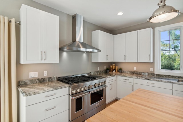 kitchen featuring white cabinets, wall chimney exhaust hood, and range with two ovens