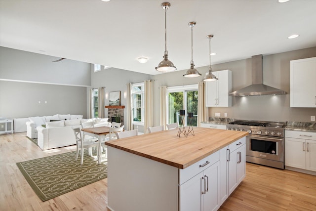 kitchen featuring wall chimney exhaust hood, butcher block countertops, high end range, and white cabinets