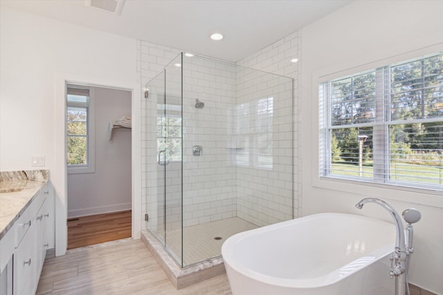 bathroom with a stall shower, visible vents, wood finished floors, vanity, and a freestanding tub