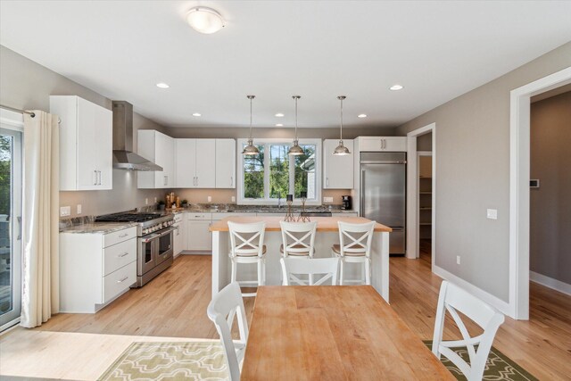 kitchen featuring wall chimney exhaust hood, premium appliances, light countertops, and light wood-style flooring