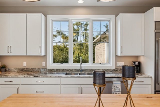 kitchen with a sink, light stone countertops, and white cabinets