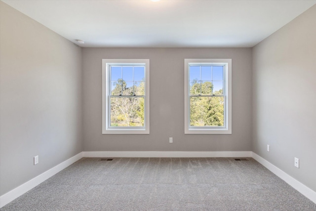 spare room featuring a wealth of natural light, carpet flooring, visible vents, and baseboards