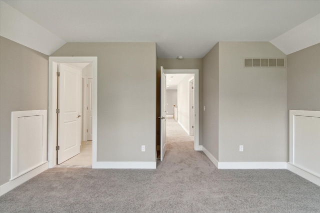 unfurnished bedroom featuring light carpet, vaulted ceiling, visible vents, and baseboards