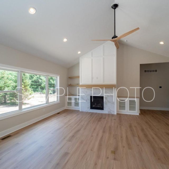 unfurnished living room with ceiling fan, light hardwood / wood-style flooring, a high end fireplace, and vaulted ceiling