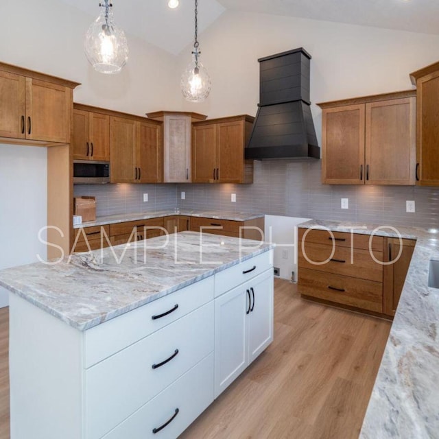 kitchen with light stone counters, backsplash, decorative light fixtures, white cabinets, and custom exhaust hood