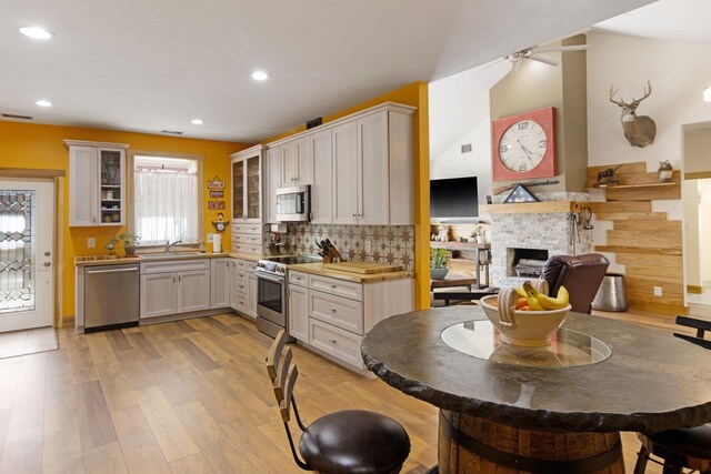 2144 N Jacobson Rd, Suttons Bay, MI 49682 - kitchen featuring appliances with stainless steel finishes, a sink, a stone fireplace, glass insert cabinets, and light wood-type flooring