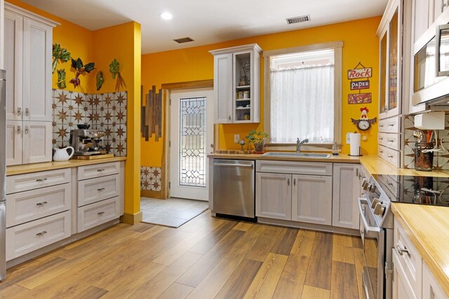 2144 N Jacobson Rd, Suttons Bay, MI 49682 - kitchen featuring butcher block countertops, appliances with stainless steel finishes, a sink, glass insert cabinets, and light wood-style floors