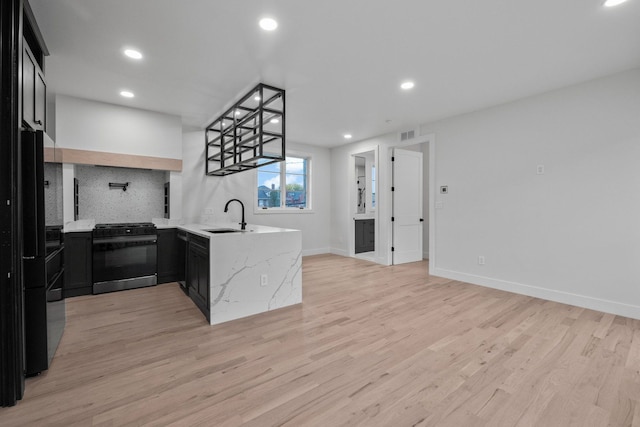 kitchen featuring light stone countertops, stainless steel range, sink, kitchen peninsula, and light hardwood / wood-style floors