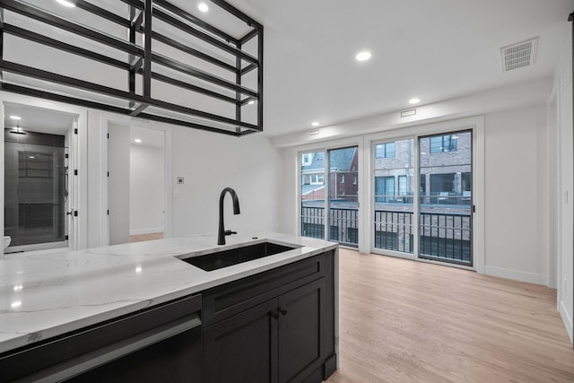 kitchen with black dishwasher, light stone countertops, light wood-type flooring, and sink