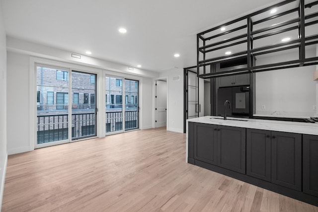 kitchen with light hardwood / wood-style floors, light stone counters, black refrigerator, and sink