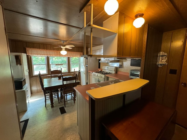 kitchen featuring wood walls, white appliances, sink, ceiling fan, and kitchen peninsula