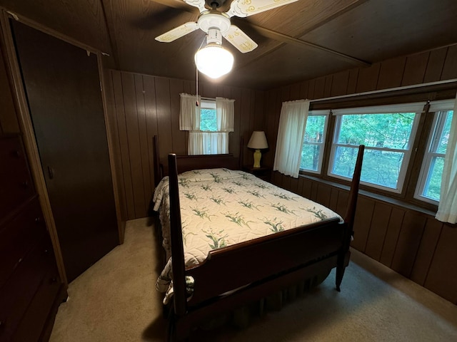 carpeted bedroom featuring ceiling fan, wooden walls, and multiple windows