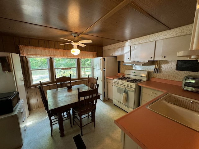 kitchen featuring ceiling fan, wood walls, white appliances, and white cabinetry