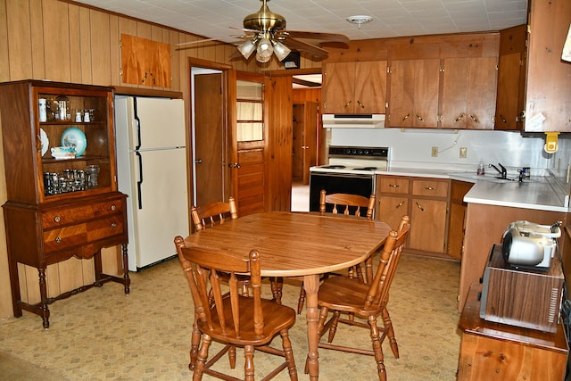 kitchen featuring white appliances, ceiling fan, wooden walls, and sink