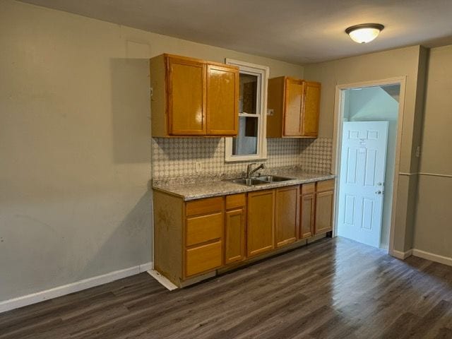 kitchen with backsplash, dark hardwood / wood-style floors, light stone counters, and sink