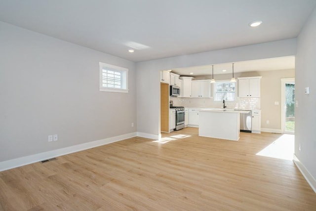 kitchen with white cabinets, appliances with stainless steel finishes, a kitchen island, light hardwood / wood-style floors, and hanging light fixtures