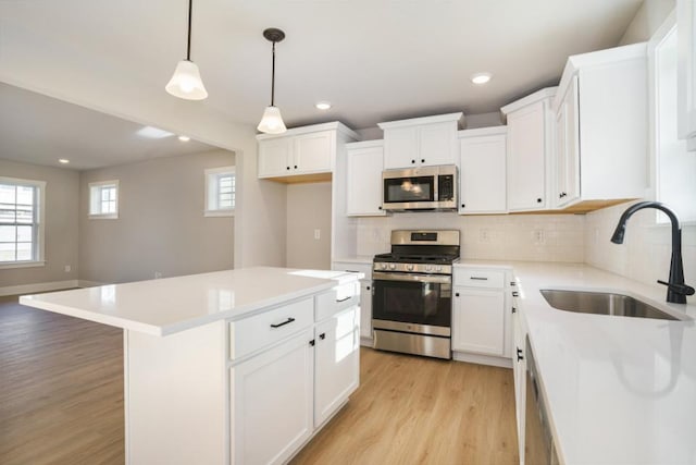 kitchen with pendant lighting, a kitchen island, sink, stainless steel appliances, and white cabinets