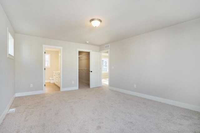 unfurnished bedroom with light colored carpet, a closet, a spacious closet, and connected bathroom