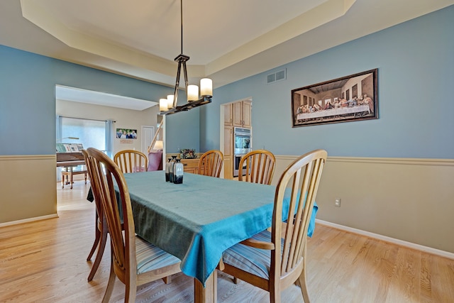 dining space featuring a raised ceiling, a chandelier, and light wood-type flooring