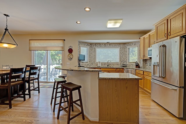 kitchen featuring stainless steel appliances, light hardwood / wood-style flooring, decorative light fixtures, decorative backsplash, and a kitchen island