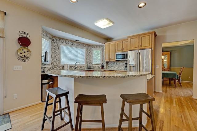 kitchen with tasteful backsplash, light stone countertops, light hardwood / wood-style flooring, and stainless steel appliances