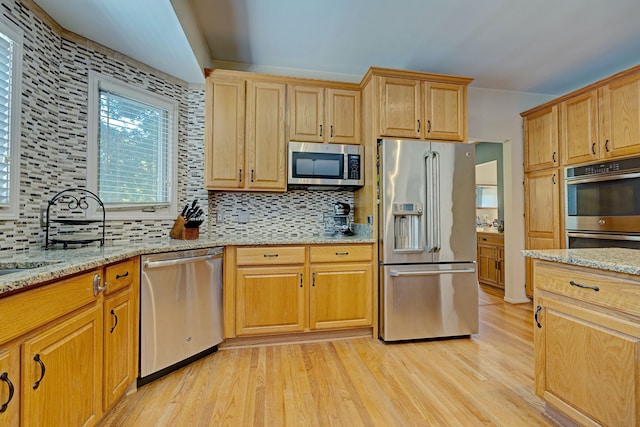 kitchen with light wood-type flooring, appliances with stainless steel finishes, backsplash, and light stone counters