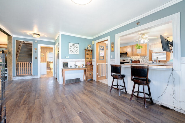 kitchen with hardwood / wood-style floors, sink, ornamental molding, kitchen peninsula, and a breakfast bar area