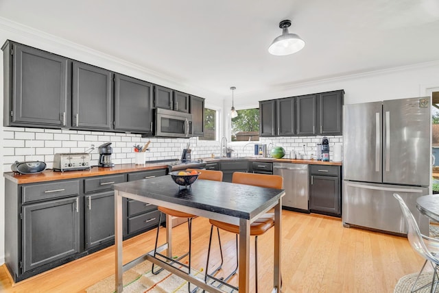 kitchen featuring backsplash, stainless steel appliances, light hardwood / wood-style floors, wood counters, and decorative light fixtures