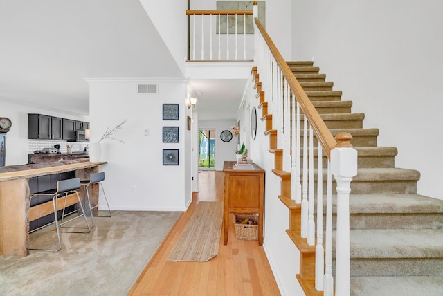 stairs with crown molding, wood-type flooring, and a towering ceiling