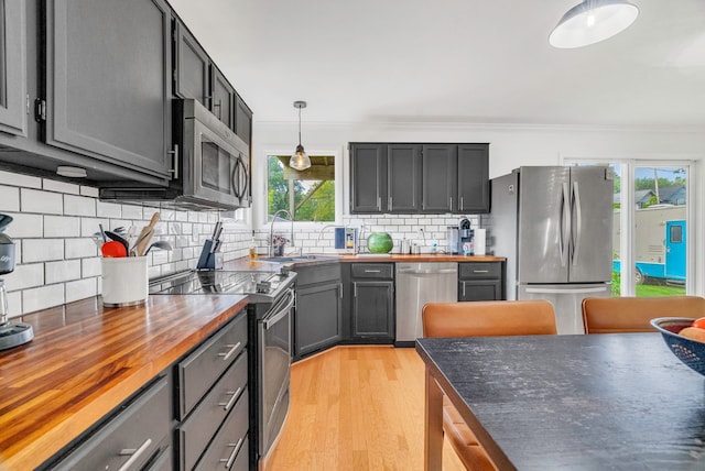 kitchen with pendant lighting, butcher block countertops, ornamental molding, and appliances with stainless steel finishes