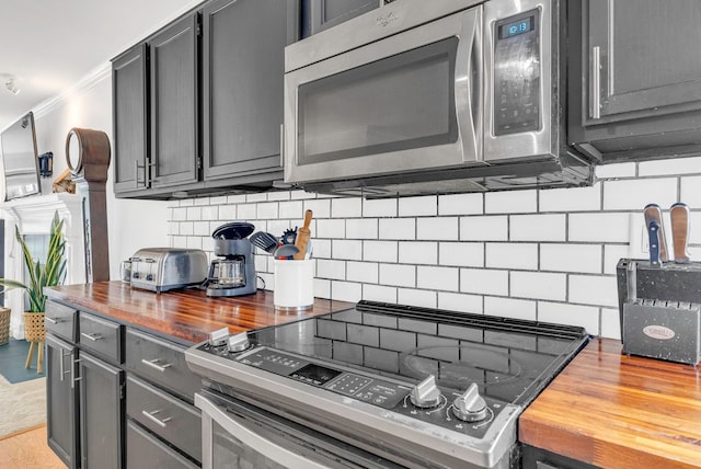 kitchen with butcher block countertops, gray cabinets, backsplash, stainless steel appliances, and ornamental molding