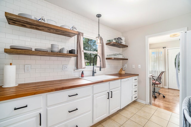 kitchen with wooden counters, pendant lighting, white cabinetry, and sink